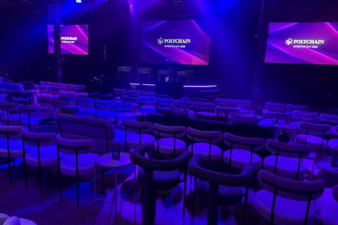 Polychain Investor Day 2025 event stage with branded screens and theater seating with purple and blue lighting