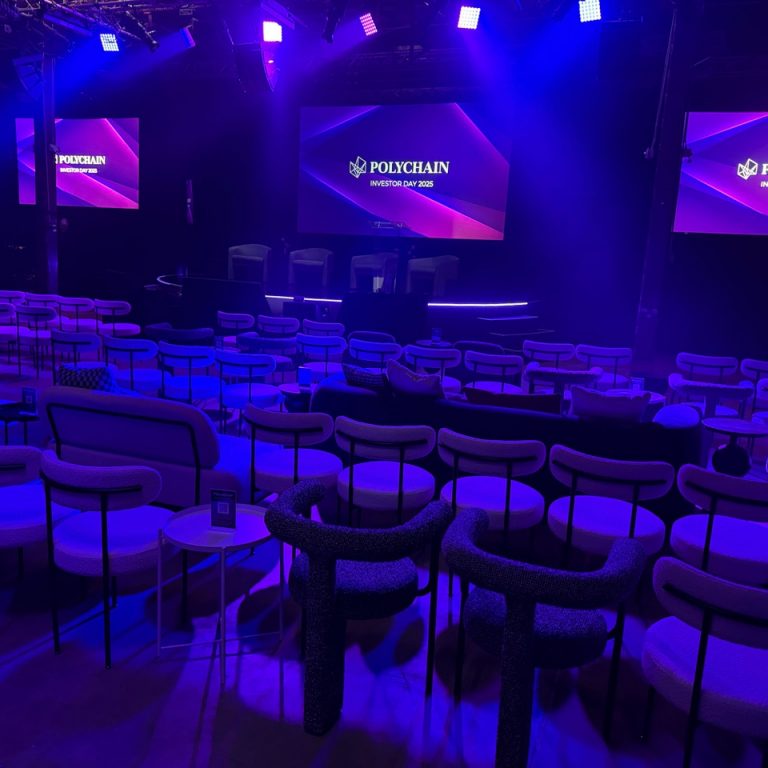 Polychain Investor Day 2025 event stage with branded screens and theater seating with purple and blue lighting