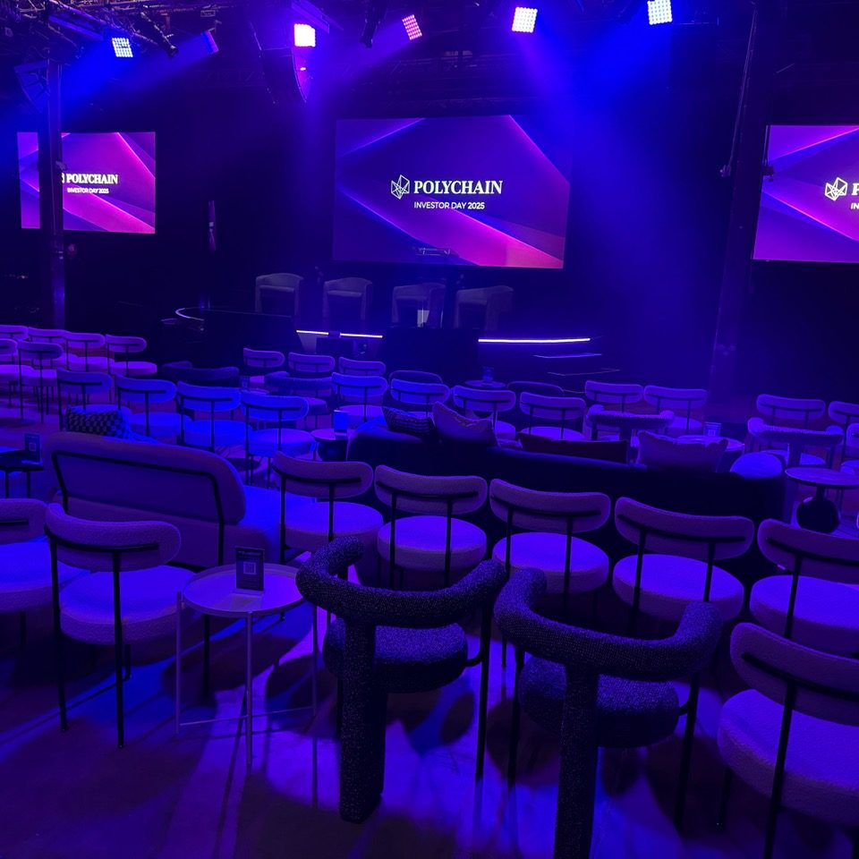 Polychain Investor Day 2025 event stage with branded screens and theater seating with purple and blue lighting